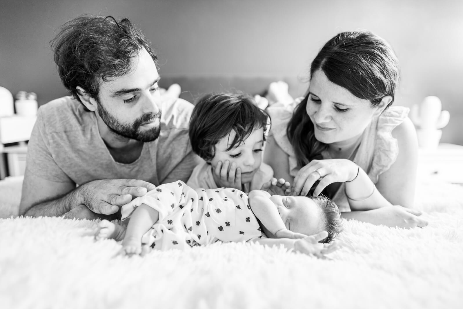 Séance photo de nouveau-né à Toulouse à domicile, portrait de famille autour de bébé endormi sur le lit