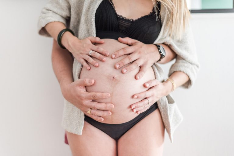 Photographe de grossesse à domicile, mains des parents sur le ventre arrondi