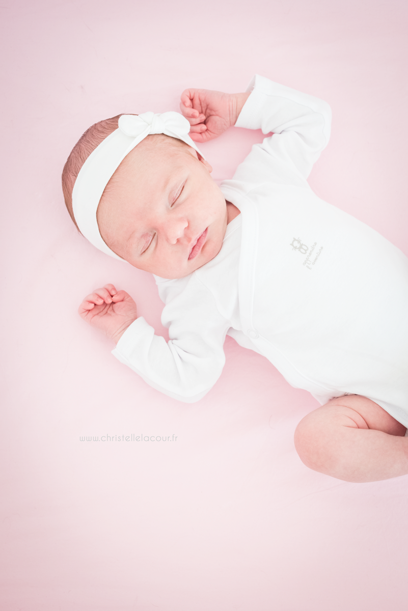 Photographe naissance à domicile, bébé adorable endormi dans son lit sur fond de rose et blanc