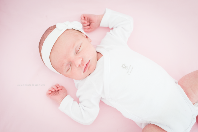 Photo nouveau-né à domicile, bébé adorable endormi dans son lit sur fond de rose et blanc