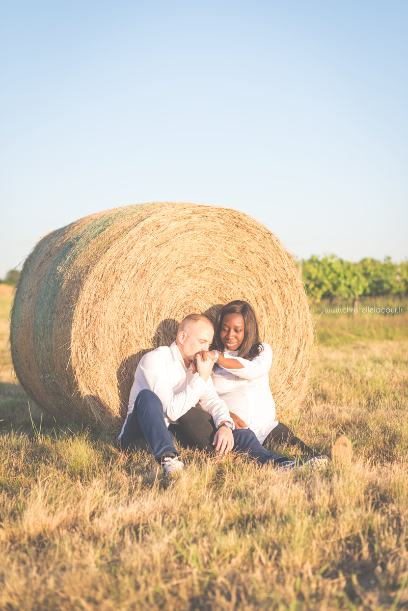 Séance grossesse à Toulouse, couple de futurs parents adossés à une botte de paille au coucher de soleil
