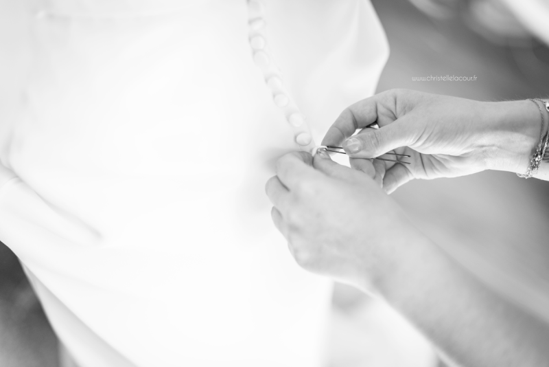 Boutonnage du dos de la robe de la mariée par la témoin, mariage fun et coloré aux Arches de la Jinolié dans le Tarn