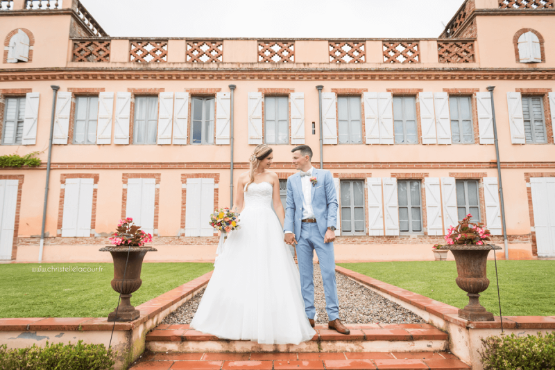 Photographe de mariage à Toulouse au Domaine Beausoleil, les mariés main dans la main devant le château en brique rose