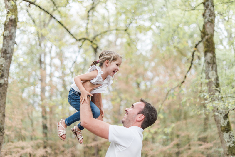 Photo d'un papa qui fait sauter sa fille lors d'une séance photo de famille en forêt de Buzet près de Toulouse
